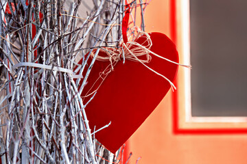 Big red heart hangs among dry branches near window. Concept of love and romance. Valentine's Day