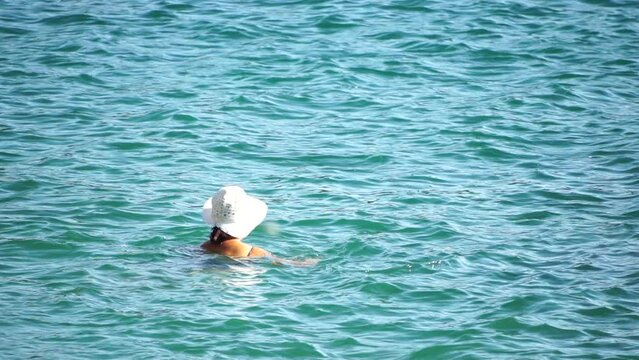 Woman swimming in calm sea at sunset, slow-motion, back view. Concept of body image and fitness, enjoying a serene beach. Happy woman with perfect fit body enjoys sea beach