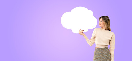 Young smiling woman holding a mockup cloud bubble on purple background