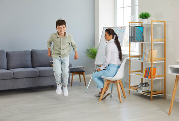 Happy little troublemaker misbehaves at a therapy session. Joyful naughty child boy jumping and having fun during a meeting with a children's therapist or psychologist. ADHD, hyperactivity concept - obrazy, fototapety, plakaty