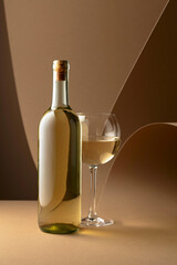 Bottle and glass of white wine on a beige background.
