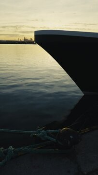 A moored ship rocks on the waves. Reflection in the water of the port on the pier in the evening. Ropes hold the white ship at the pier. Spain. Grao, Castellon