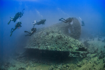 Underwater scene with scuba divers exploring an ancient shipwreck, illuminated by natural light in clear blue water, ideal for adventure and diving themes