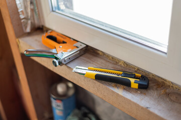 a construction stapler and a construction knife lie on the window sill of an installed plastic...
