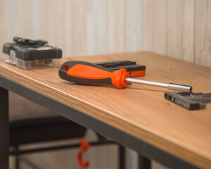 a screwdriver with replaceable bits with an orange handle lies on the table next to a box with a...