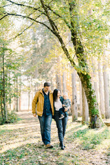 Smiling dad hugs mom with a little girl in her arms walking through the forest