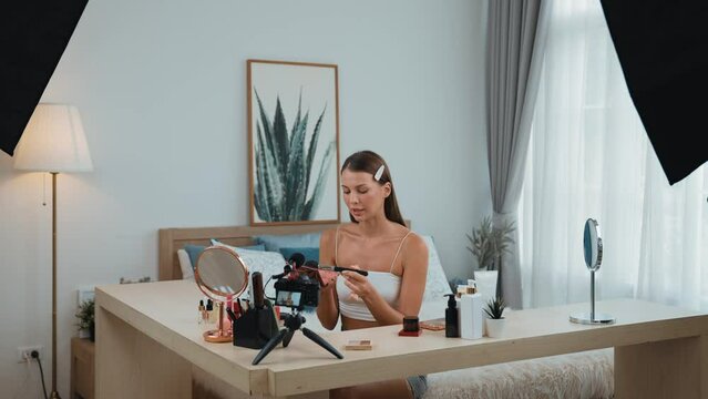 Young woman making beauty and cosmetic tutorial video content for social media. Beauty blogger smiles to camera while showing how to beauty care to audience or followers. Adit