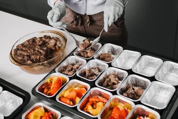 Poster Meal Prep Service: Portioning Healthy Meat and Vegetables. A meal prep worker portions nutritious beef and colorful bell peppers into individual trays, preparing well-balanced office lunches. © irissca