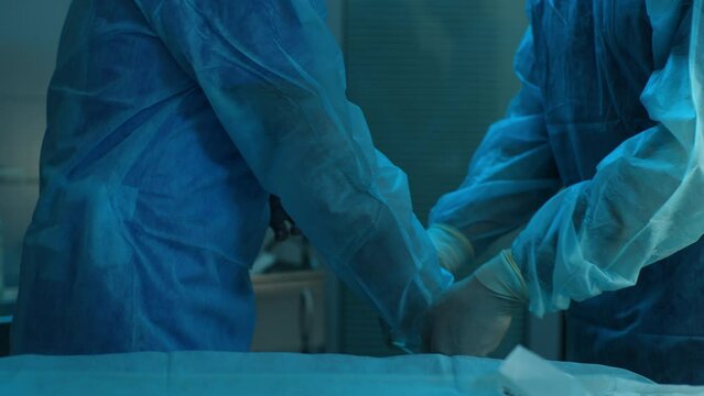 Close-up hands of unrecognizable assistant helping surgeon put on latex gloves before operation. Closeup of team of surgeons in operating room preparing for surgery. Shooting in slow motion.