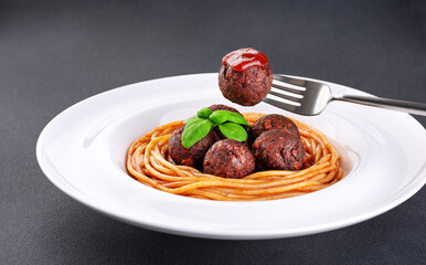 Fried vegan meatballs with noodles and basil leaves on a plate. Fork with a meatball and ketchup.