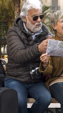 Vertical video. Middle aged heterosexual couple tourists looking at a map in a city during vacation