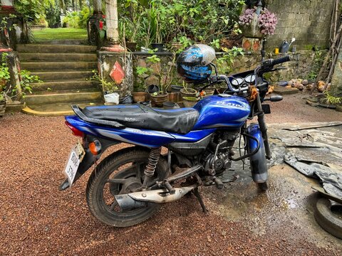 wet Bajaj Platina 100 ES motorcycle from 2015 parked in a rural street, Sri Lanka