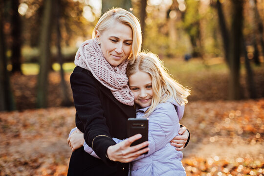 Parent-child bonds and mother daughter relationships. Mother and daughter embracing, capturing a special moment selfie together amidst the golden hues of autumn.