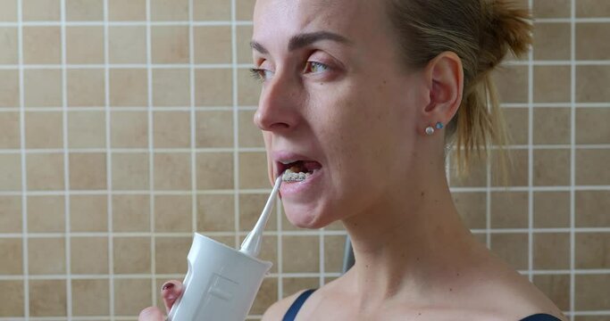 Young woman cleaning her teeth with brace by oral irrigator.