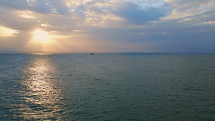 Aerial breathtaking ocean sunrise with lonely boat floating on gloomy horizon.