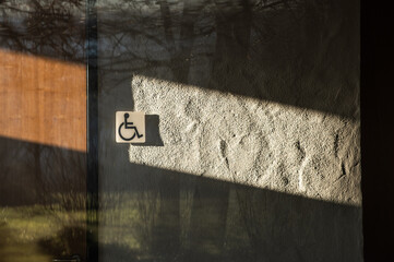 Symbol Rollstuhlfahrer an Toiletten-Holztüre und verputzter Wand mit Schattenspiel mit starkem...