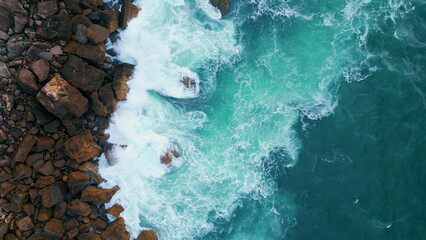 Sea splashing coastal stones aerial view. Ocean water breaking rocks seashore.