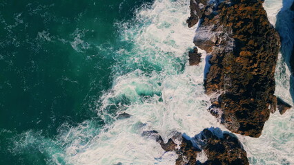 Foamy ocean water splashing on coastal crag aerial view. Waves crashing rocks.