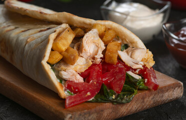 A delicious  doner kebab wrap with  meat, lettuce, tomato, onion and sauce on black background.