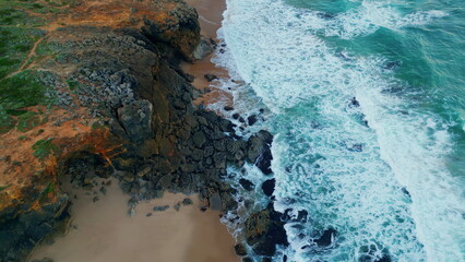 Foamy sea waves washing rocky seashore in slow motion. Aerial view stormy ocean.