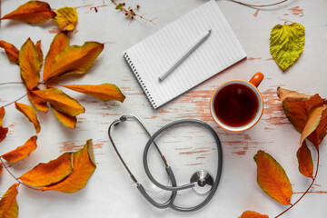Top view of hot coffee served on shabby table with stethoscope and scattered yellow leaves ,autumn composition