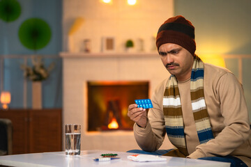 Middle aged sick man in winter wear checking pills prescription or dosage before taking at home -...