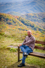 Naklejka na ściany i meble Serene Man Sitting on Wooden Bench Enjoying Scenic View of Majestic Mountain Landscape