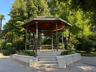 Picturesque outdoor gazebo with a wooden bench and steps, set in a lush green garden