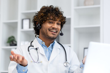 Young Indian doctor consulting patients remotely, man in white medical coat with headset using...
