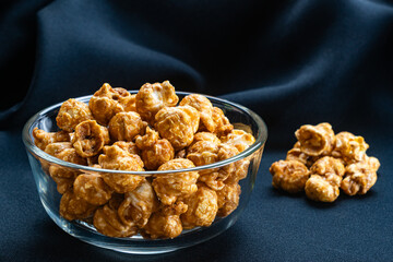 View of sweet caramel almonds in transparent glass bowl on black cloth background.