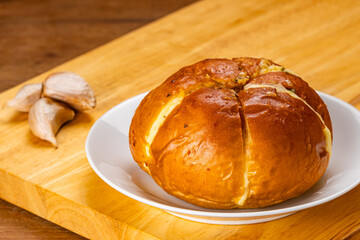 High angle view of korean cream cheese garlic bread in white ceramic dish with raw garlic on wooden board on wooden background.