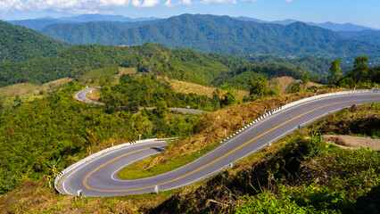The green mountains are cut by a curved road.