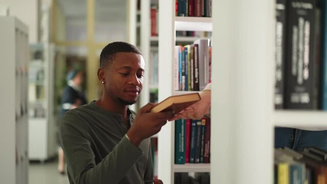 Student receives books in public library. Black man takes folio from librarian visiting university information center. Literature for essay writing