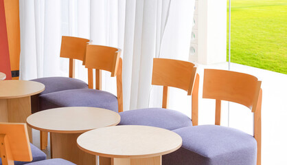 Row of wooden beige dining round table sets with chairs near white curtain on glass wall inside of modern coffee shop, perspective side view 