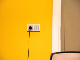Gray electrical socket on yellow wall and charger plugged into the socket at working room.Proper use of sustainable energy sources. Clean energy.Close up shot. 
