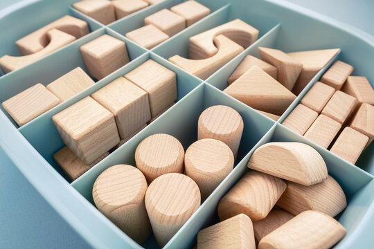 Many wooden geometric toys are kept in the same types of storage box, organization box with partitions, category concept
