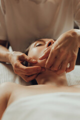 Obraz na płótnie Canvas Hands of female chiropractor massaging face of young woman lying on massage table. Visceral massage. Concept of physical therapy treatment, neck pressure point