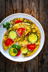 Omelette - scrambled eggs with mozzarella cheese, zucchini and tomatoes on wooden table
