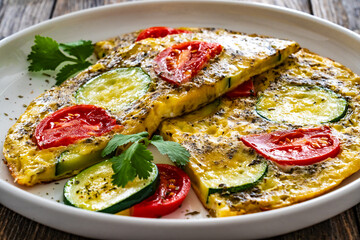 Omelette - scrambled eggs with mozzarella cheese, zucchini and tomatoes on wooden table
