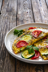 Omelette - scrambled eggs with mozzarella cheese, zucchini and tomatoes on wooden table
