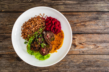 Wrapped beef in sauce served with boiled buckwheat and grated beets on wooden table
