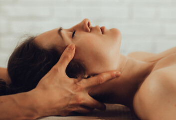 Hands of female chiropractor massaging face of young woman lying on massage table. Visceral...