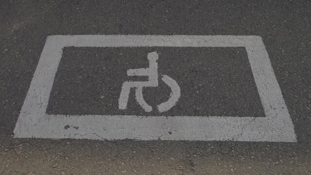 Road sign parking for disabled painted with white paint on asphalt in parking lot on city street