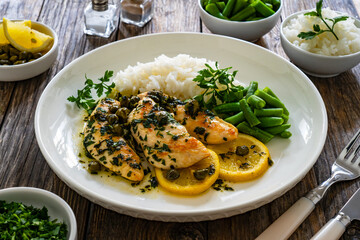Chicken piccata with white rice and capers in sauce on wooden background
