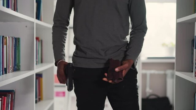 Man takes gun off holster in bookstore closeup. Armed robber prepares to assault college library customers. African American security guy at work