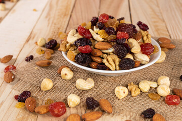 Assorted nuts and dried fruits, almonds, cashews, hazelnuts or filbert, walnuts, light and dark raisins, dried cherries and cranberries in a white bowl on a wooden background.