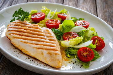 Grilled chicken breast and fresh vegetables on wooden table
