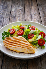 Grilled chicken breast and fresh vegetables on wooden table
