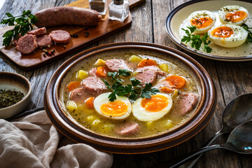  Sour rye soup with sausages and boiled eggs on wooden table