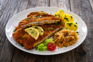 Crispy breaded fried cutlet with boiled potatoes and cooked cabbage on wooden table

